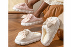 Pink and white slippers with bow details on a wooden floor.