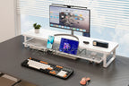 White desk setup with computer monitor, keyboard, mouse, and smartphone on a blurred window background.